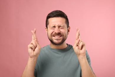 Emotional man crossing his fingers on pink background