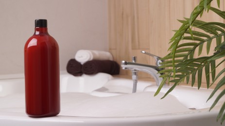 Photo of Red bottle of bath foam and towels on tub indoors, space for text
