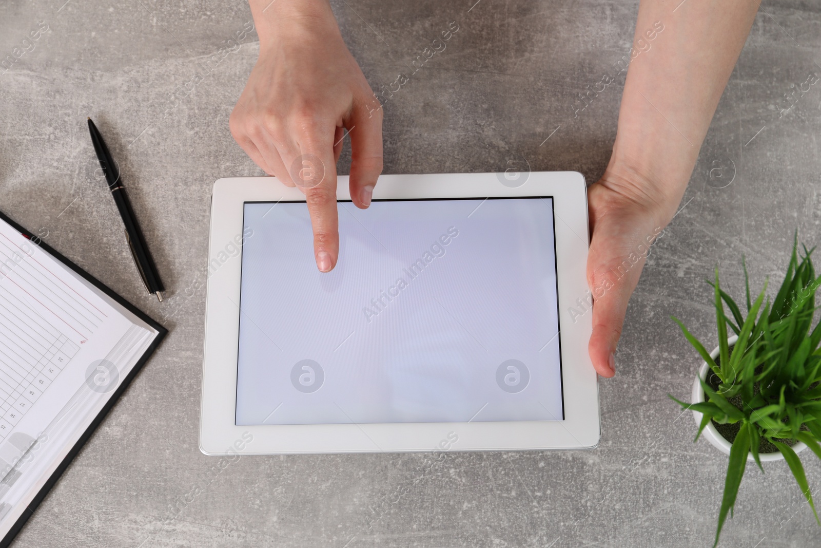 Photo of Woman using tablet with blank screen at grey stone table, top view. Space for text