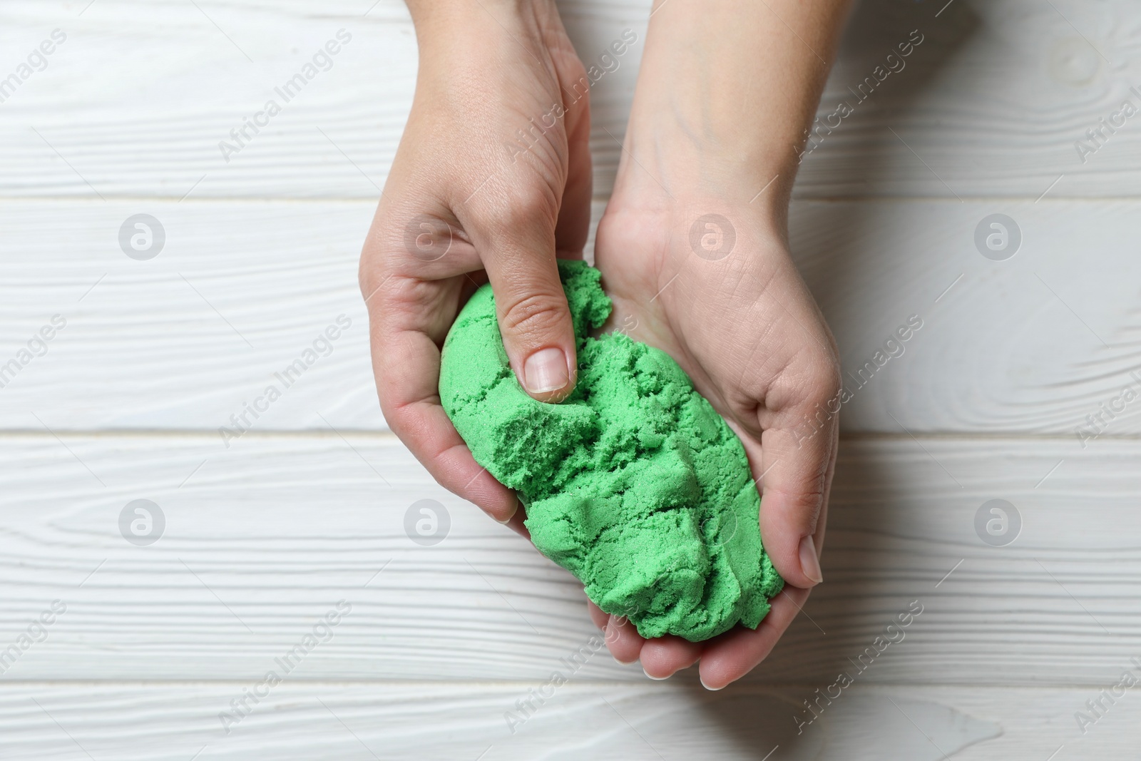 Photo of Woman playing with green kinetic sand at white wooden table, top view