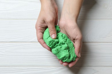 Woman playing with green kinetic sand at white wooden table, top view