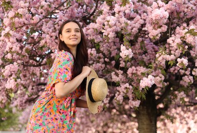 Beautiful woman with straw hat near blossoming tree on spring day