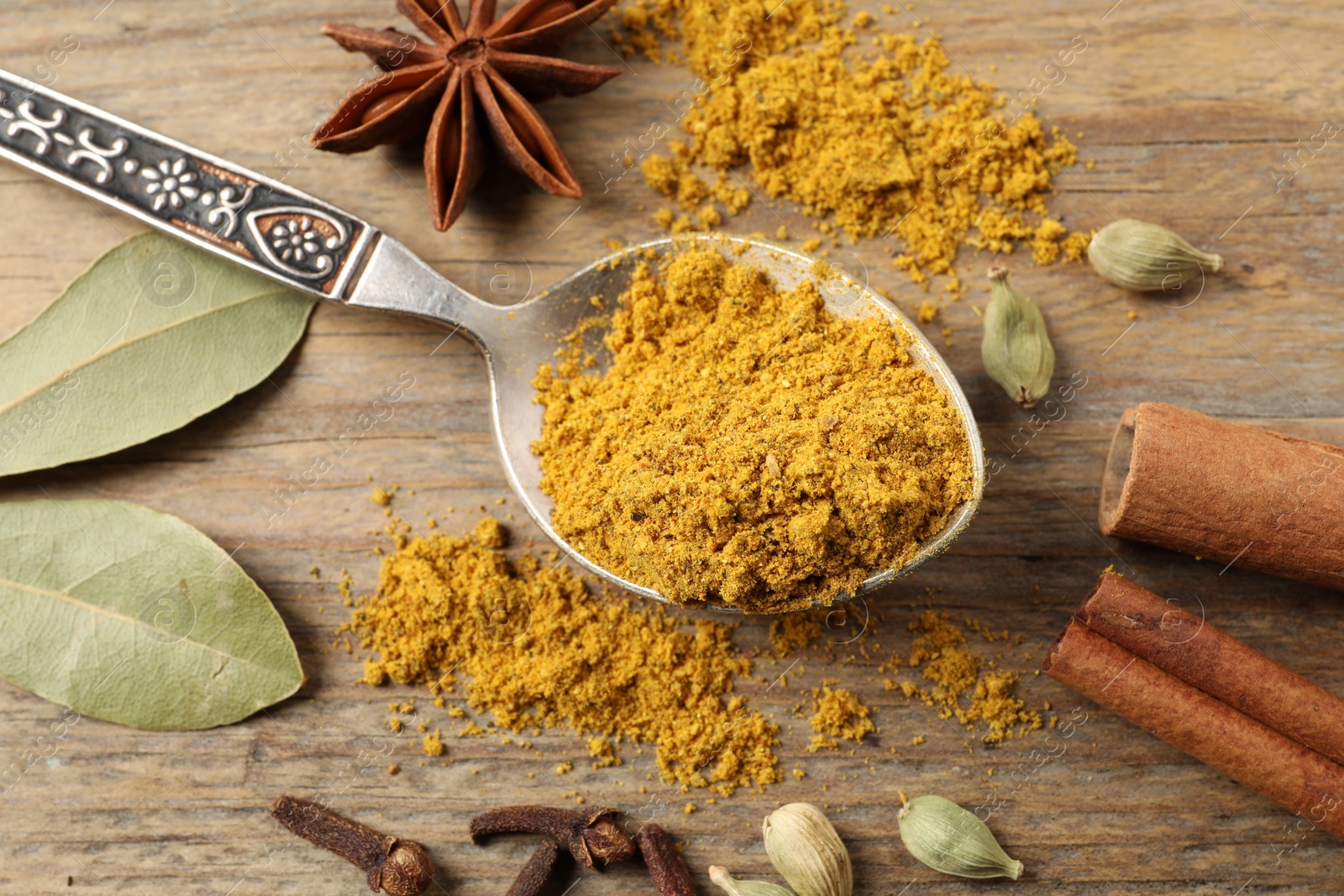 Photo of Spoon with dry curry powder and other spices on wooden table, flat lay