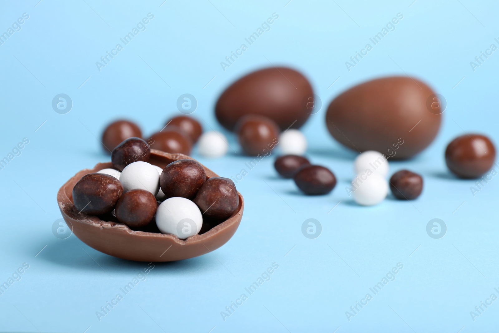 Photo of Tasty chocolate eggs with different sweets on light blue background. Space for text