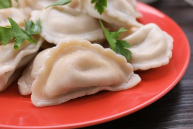 Photo of Delicious dumplings (varenyky) with potatoes and parsley on brown wooden table, closeup