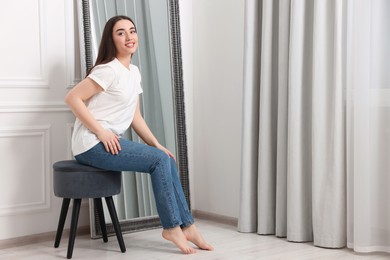 Photo of Young woman in stylish jeans near mirror indoors. Space for text