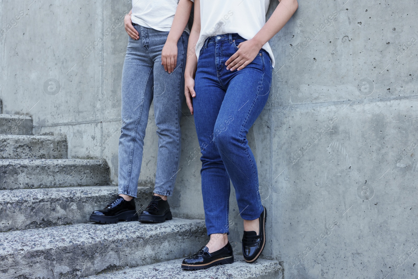 Photo of Women in stylish jeans on stairs near stone wall outdoors, closeup