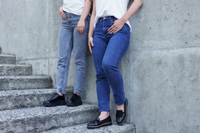 Photo of Women in stylish jeans on stairs near stone wall outdoors, closeup