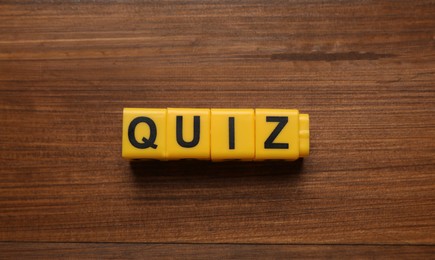 Yellow cubes with word Quiz on wooden table, flat lay