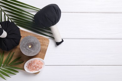 Beautiful spa composition with herbal massage bags, burning candle and leaves on white wooden table, flat lay. Space for text