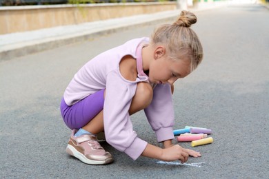 Photo of Little child drawing butterfly with chalk on asphalt