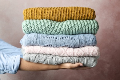 Photo of Woman holding stack of warm clothes on pink background, closeup. Autumn season