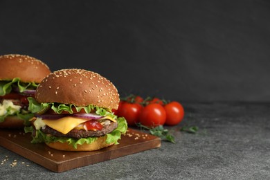 Photo of Delicious burgers with beef patty and tomatoes on grey table, space for text
