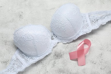 Photo of Pink ribbon and bra on white textured table, top view. Breast cancer awareness