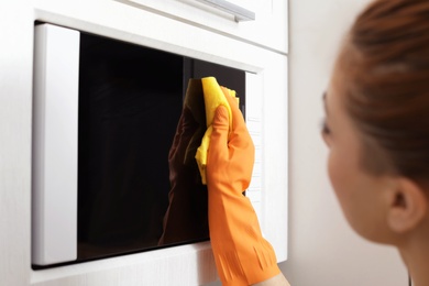 Photo of Woman cleaning microwave oven with rag in kitchen