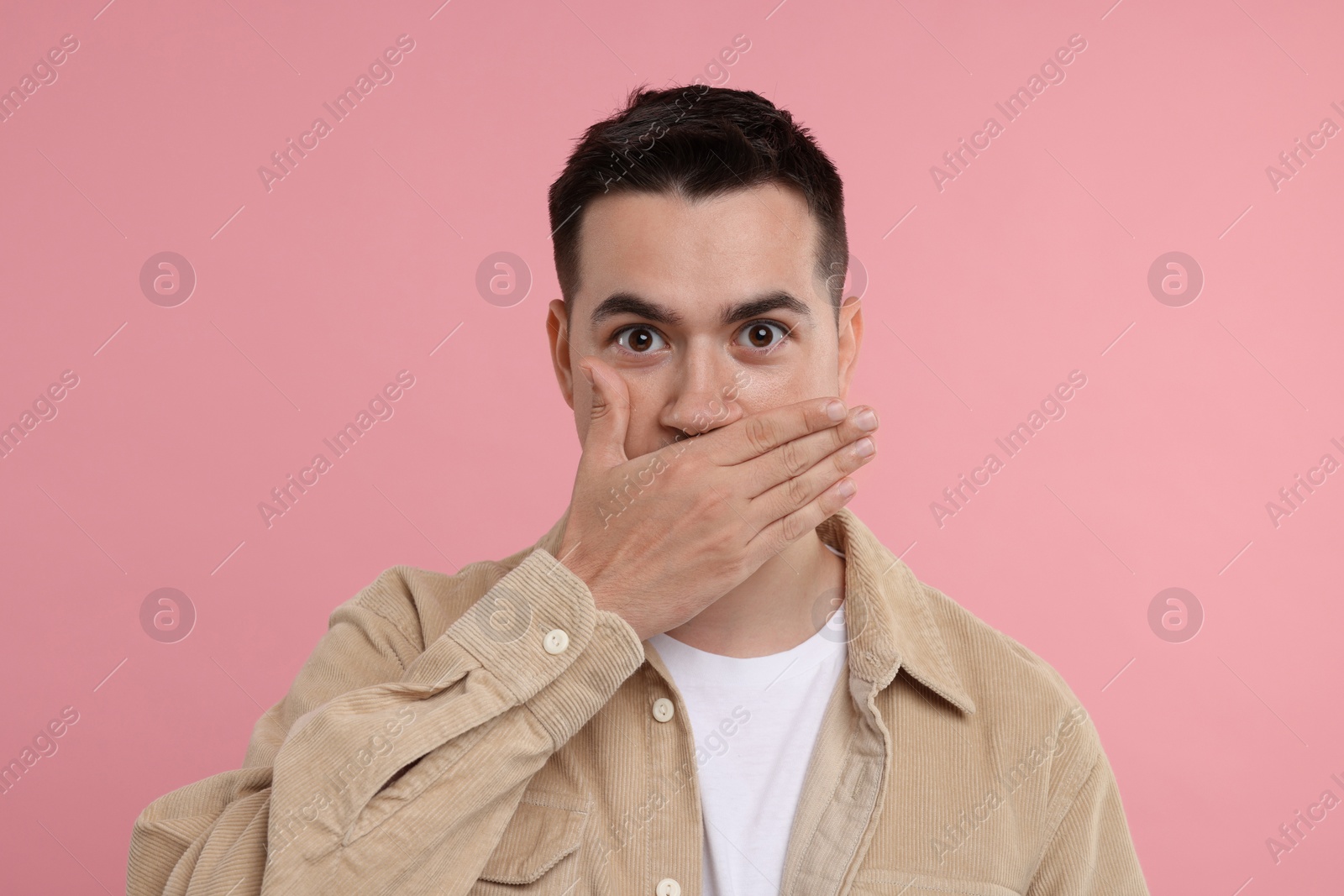 Photo of Embarrassed man covering mouth with hand on pink background