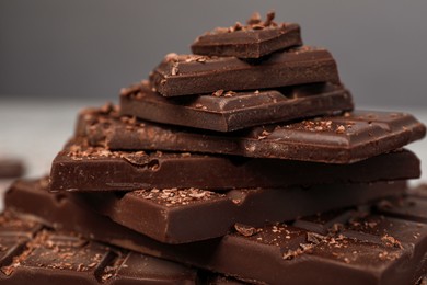 Photo of Pieces and shavings of tasty chocolate on blurred background, closeup