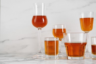 Different delicious liqueurs in glasses on white marble table, space for text