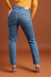 Photo of Woman in stylish jeans on brown background, closeup