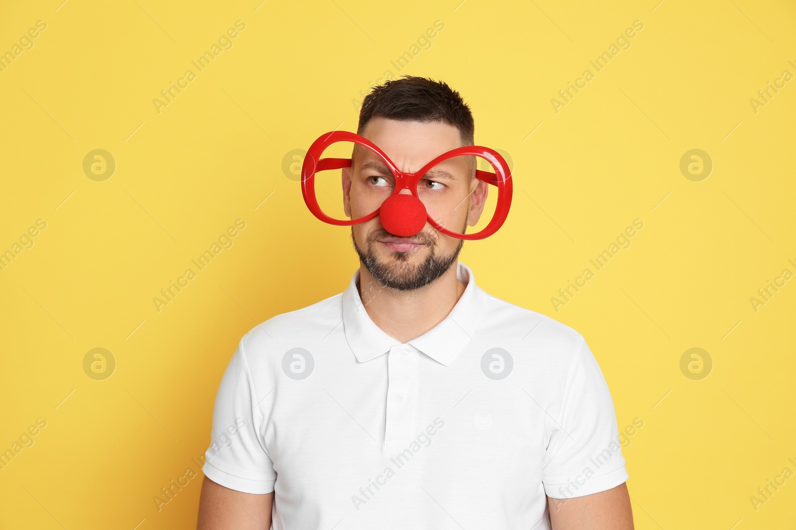 Photo of Man with clown nose and funny glasses on yellow background. April fool's day