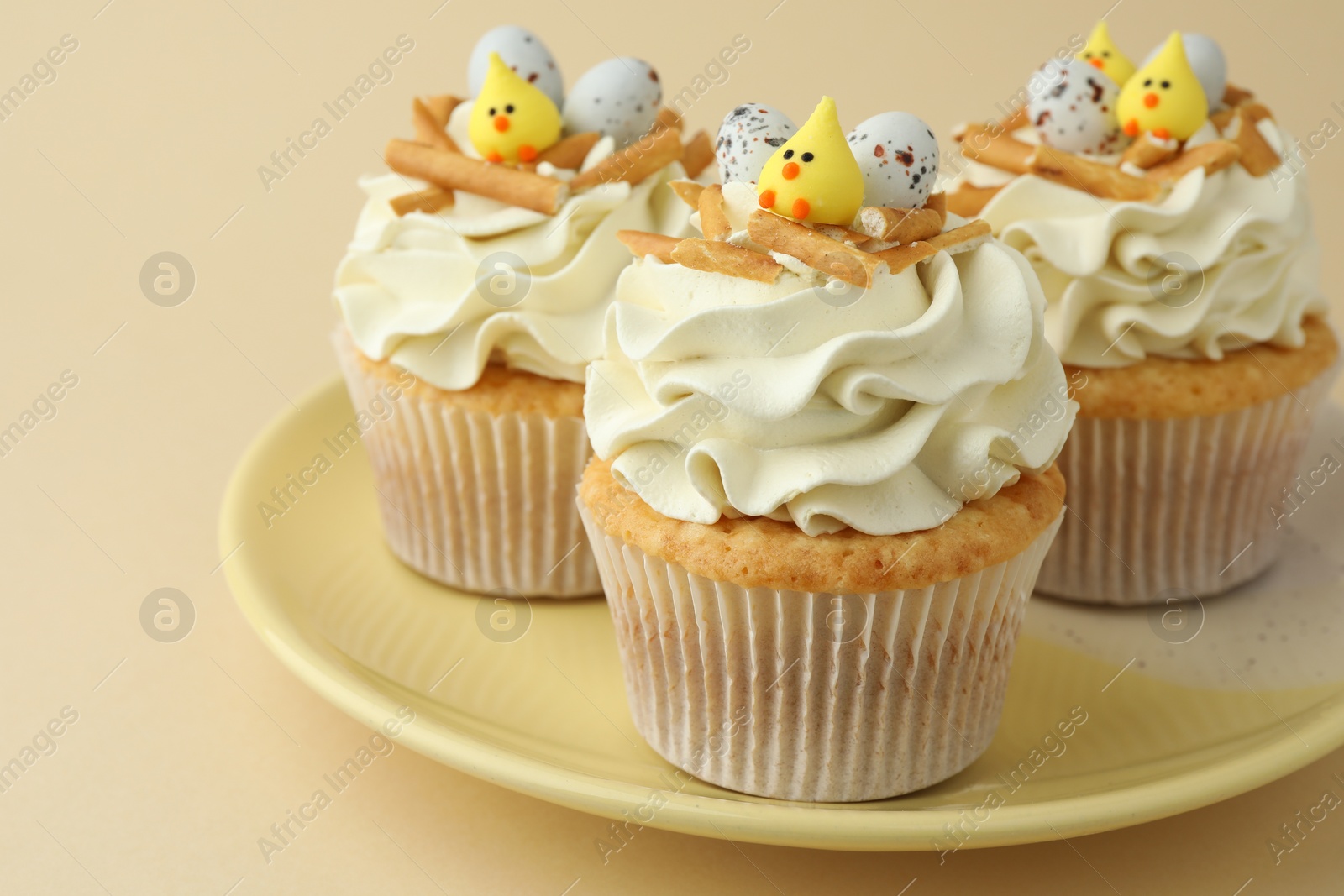 Photo of Tasty Easter cupcakes with vanilla cream on beige background, closeup