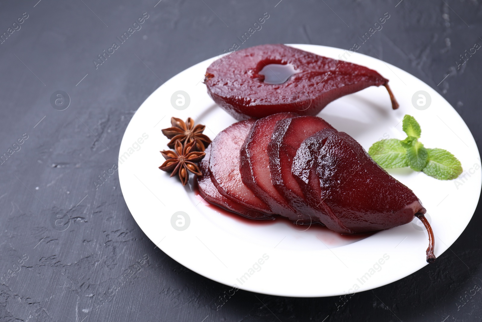 Photo of Tasty red wine poached pears, mint and anise on black table, closeup