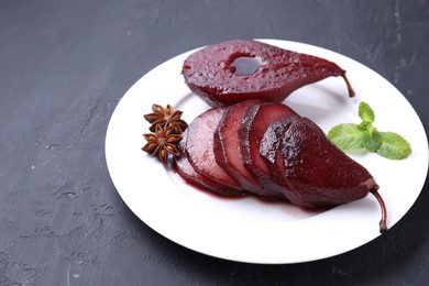 Tasty red wine poached pears, mint and anise on black table, closeup