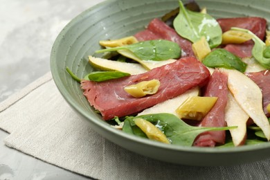 Photo of Delicious bresaola salad in bowl on light textured table, closeup