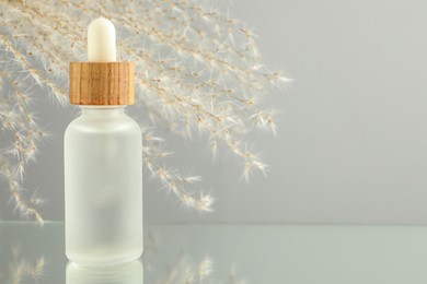 Bottle of face serum and beautiful dried flowers on light grey background, closeup. Space for text