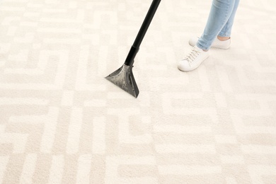 Woman removing dirt from carpet with vacuum cleaner indoors, closeup. Space for text