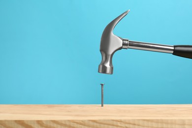 Photo of Hammering nail into wooden surface against light blue background