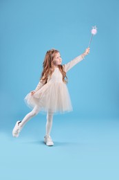 Cute girl in fairy dress with diadem and magic wand on light blue background. Little princess