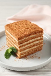 Photo of Slicedelicious layered honey cake with mint served on white wooden table, closeup