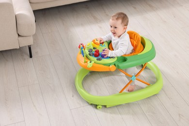 Photo of Cute little boy making first steps with baby walker indoors