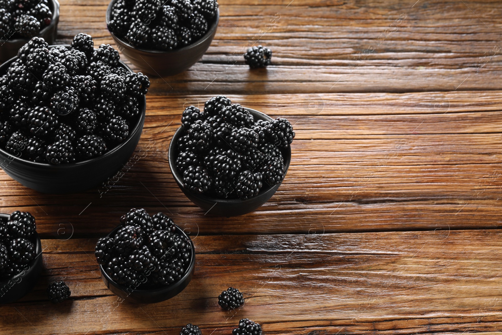 Photo of Ripe blackberries in bowls on wooden table, space for text
