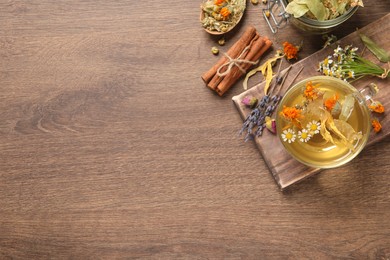 Freshly brewed tea and dried herbs on wooden table, flat lay. Space for text