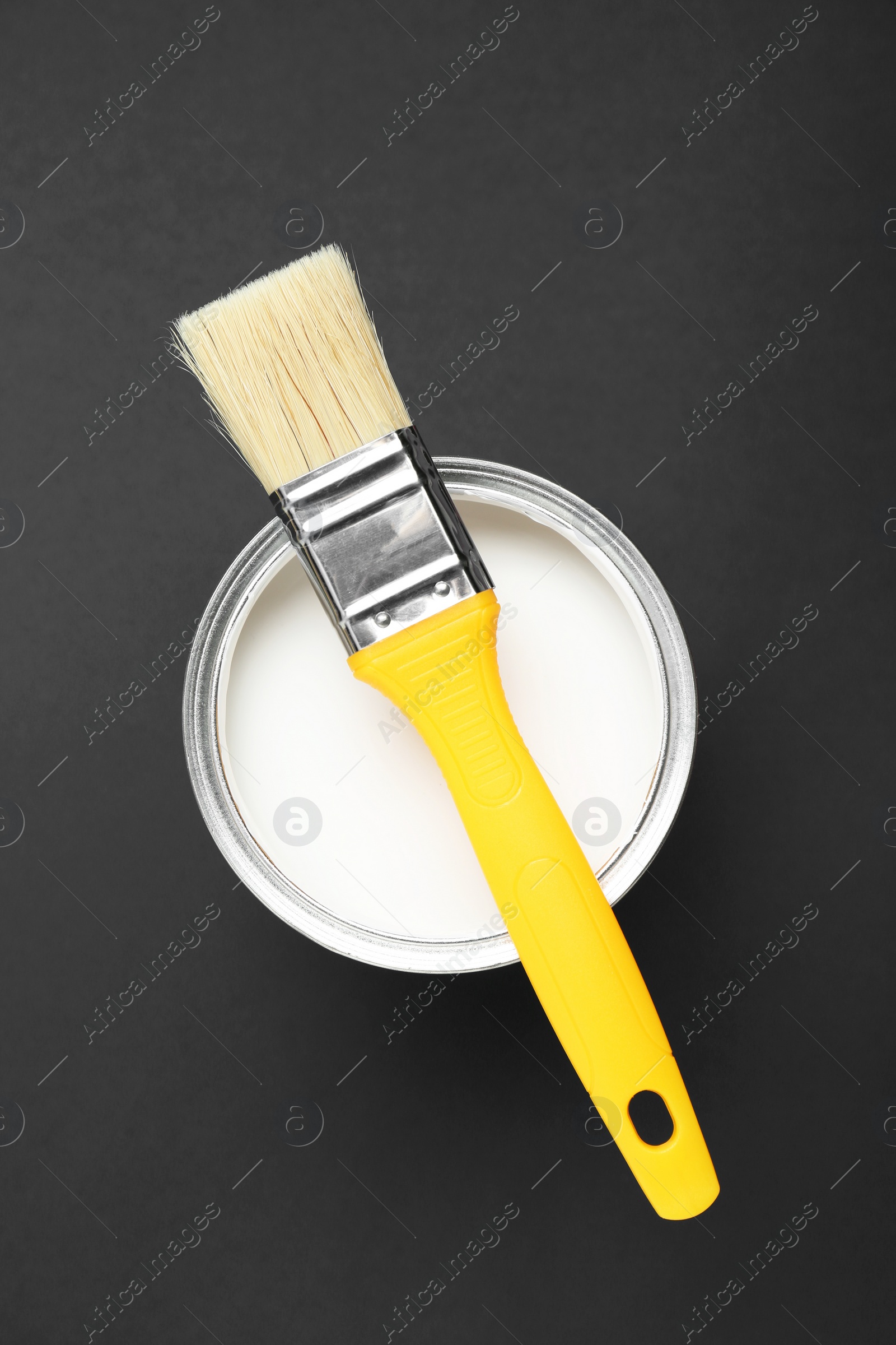 Photo of Can of white paint with brush on black background, top view