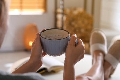 Woman with cup of aromatic coffee relaxing at home, closeup