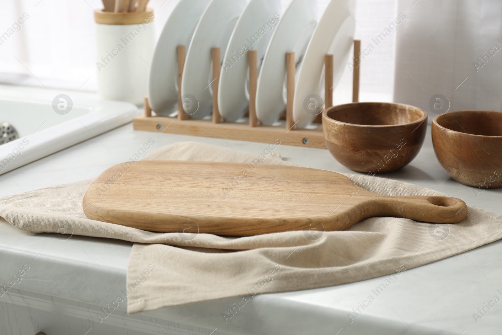 Photo of Wooden cutting board, dishware and towel on white countertop in kitchen