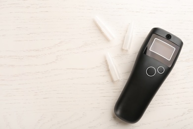 Modern breathalyzer with blank screen and mouthpieces on white wooden table, flat lay. Space for text