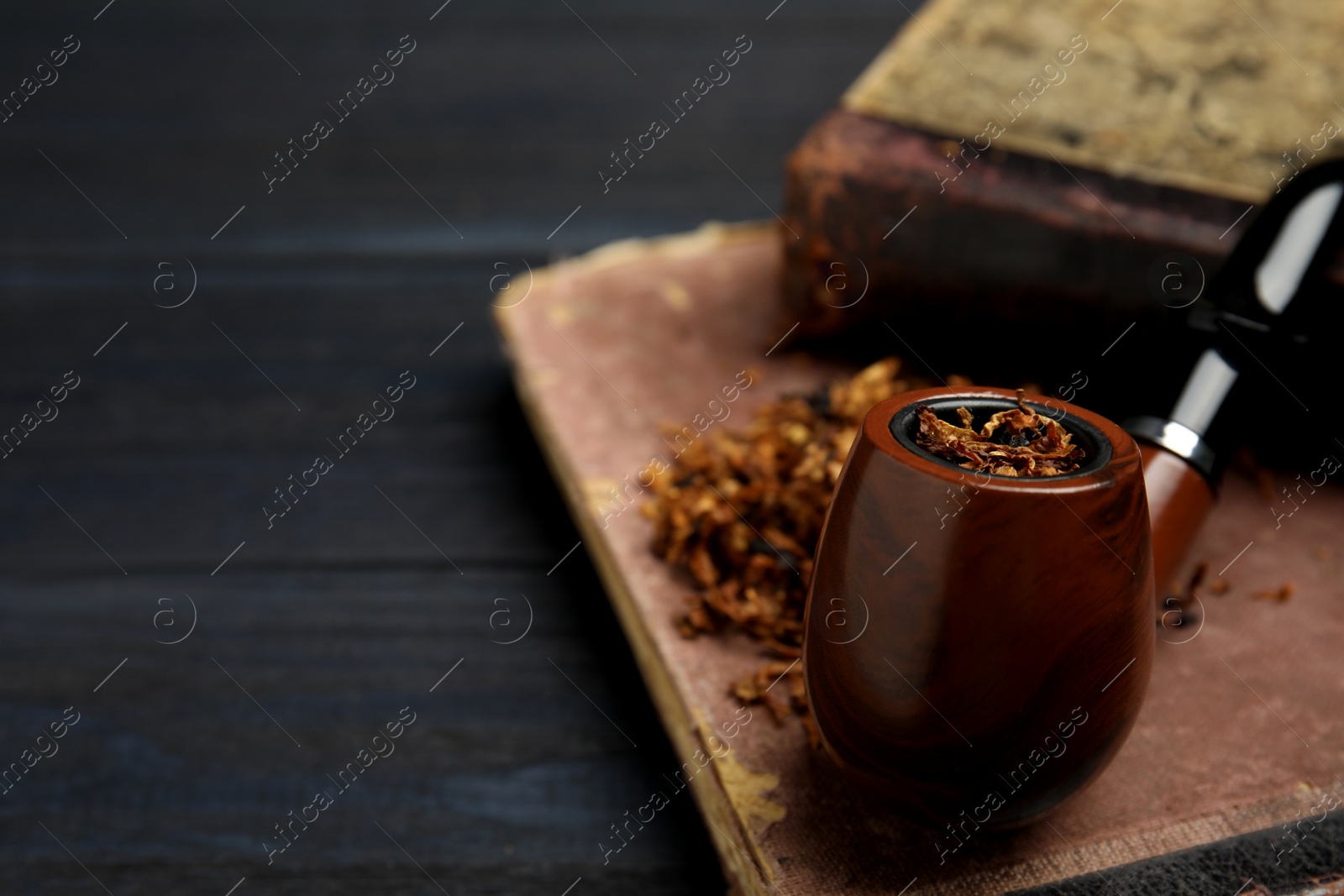 Photo of Smoking pipe, dry tobacco and old books on black table, closeup. Space for text