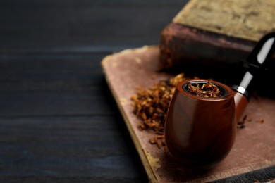 Photo of Smoking pipe, dry tobacco and old books on black table, closeup. Space for text