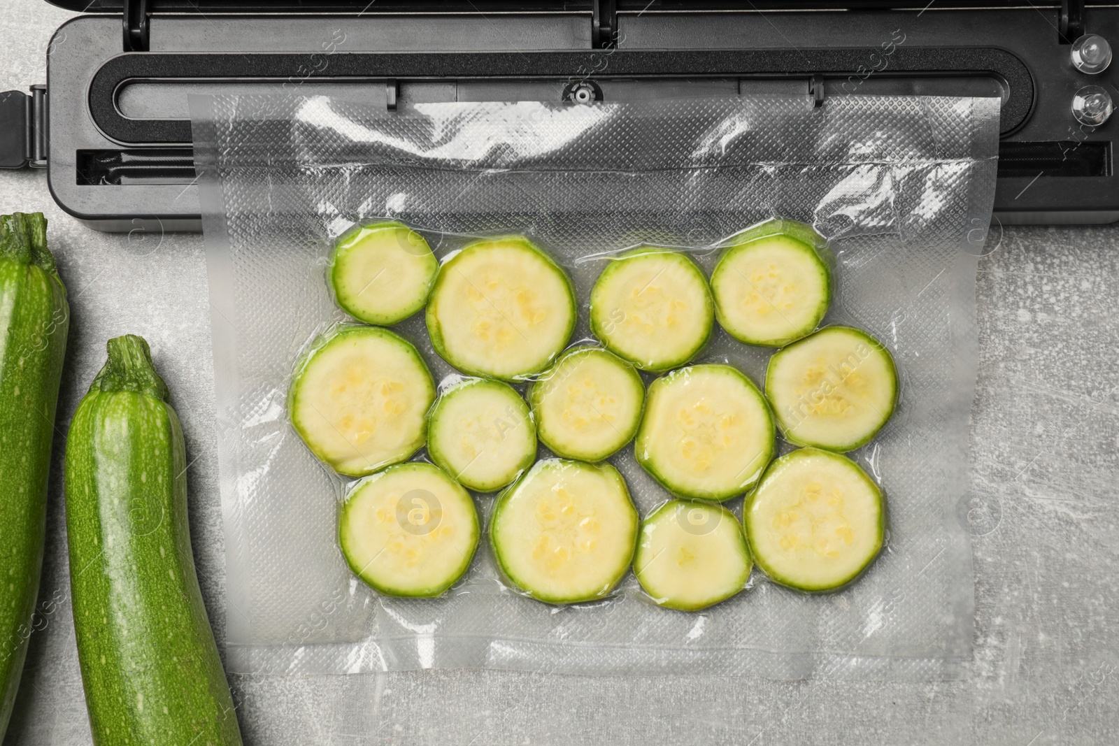 Photo of Sealer for vacuum packing with plastic bag of zucchini on light grey table, top view