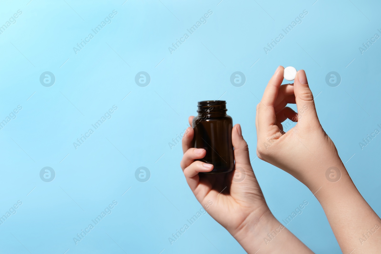 Photo of Woman holding pill and bottle on light blue background, closeup. Space for text