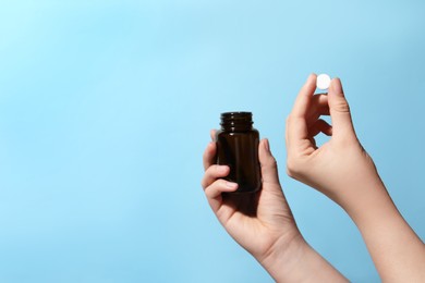 Woman holding pill and bottle on light blue background, closeup. Space for text