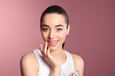 Photo of Young woman applying balm on her lips against color background