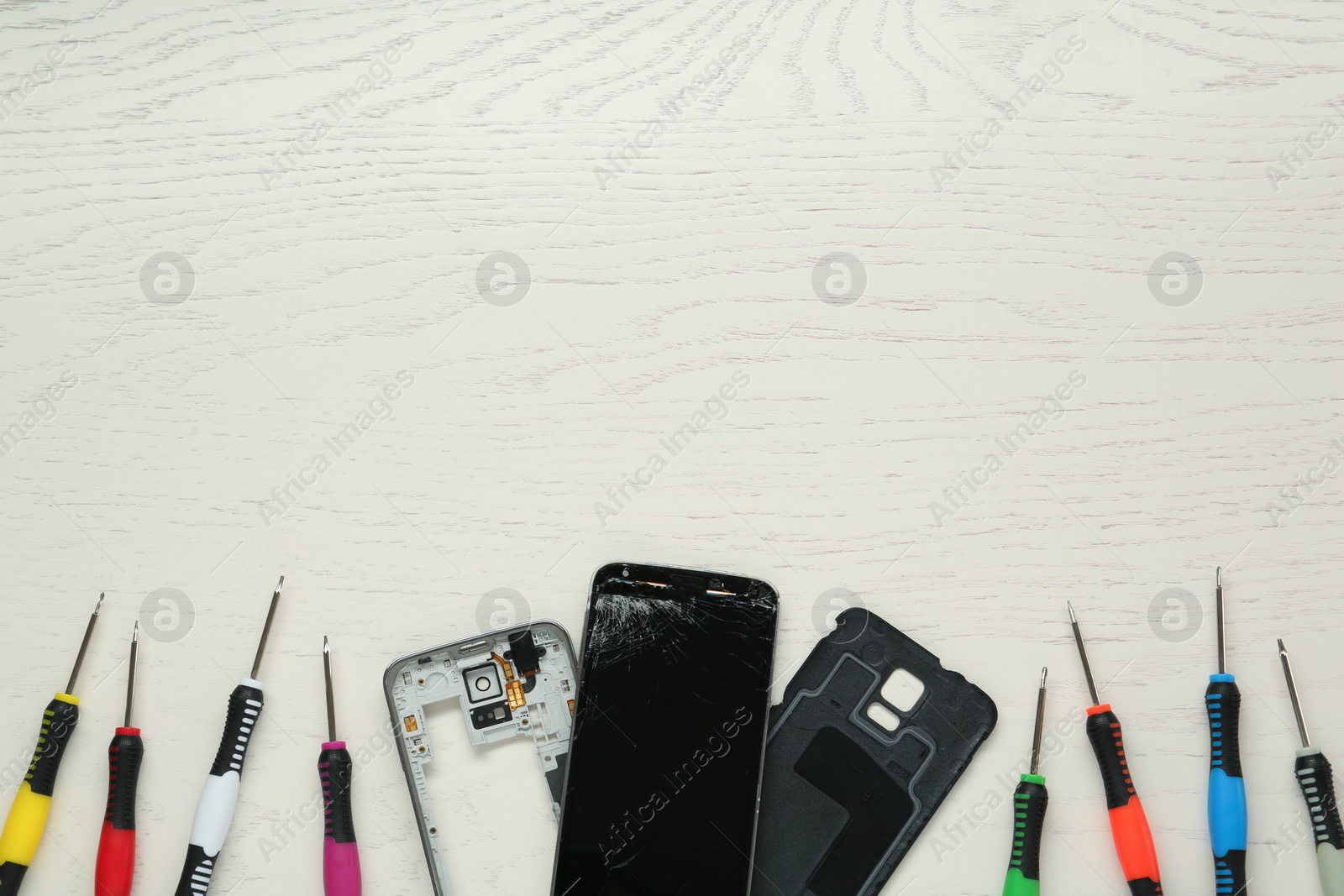 Photo of Damaged smartphone and repair tool set on light beige wooden table, flat lay. Space for text