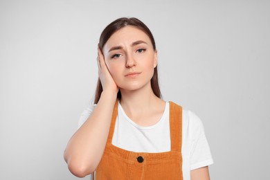 Young woman suffering from ear pain on light grey background