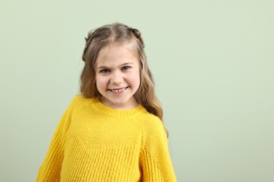 Cute little girl with braided hair on light green background. Space for text
