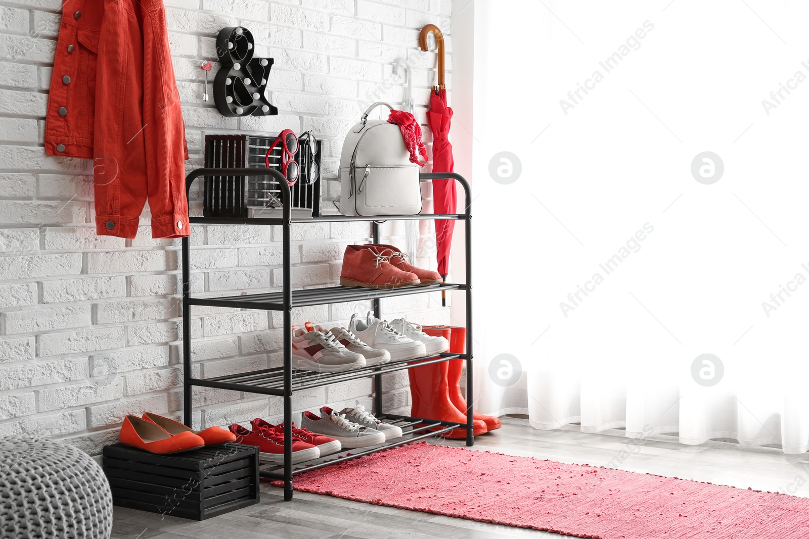 Photo of Shelving rack with stylish women's shoes and accessories near white brick wall indoors